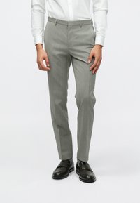 Ανοιχτό γκρι, στενές παντελόνες με διακριτές κατακόρυφες ρίγες. Διαθέτουν θηλιές ζώνης, πλαϊνές τσέπες και λεία υφή. Συνδυάζονται με μαύρες loafers.