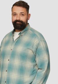 Koszula zapinana na guziki w kratkę w odcieniach niebiesko-zielonym i kremowym. Posiada kołnierzyk i długie rękawy, wykonana z miękkiego materiału.