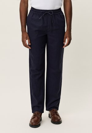 Pantalon bleu marine avec cordon de serrage en coton, coupe décontractée. Associé à des chaussures à lacets marron texturées avec une semelle robuste.