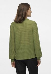 Grøn, struktureret bluse med lange ærmer, prydet med et zigzag-mønster og en rund halsudskæring. Sammen med sorte bukser.