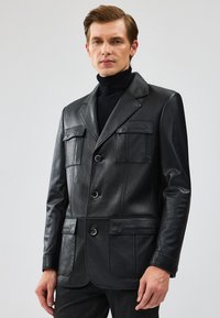 Zwarte leren blazer met twee borstzakken, twee voorzakken en een sluiting met drie knopen. Heeft een gladde textuur en een getailleerde pasvorm.