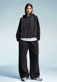 Czarna, oversize bluza z kapturem, z kieszenią z przodu i sznurkiem, nakładana na biały t-shirt. Połączona z luźnymi czarnymi spodniami i szarymi butami sportowymi.