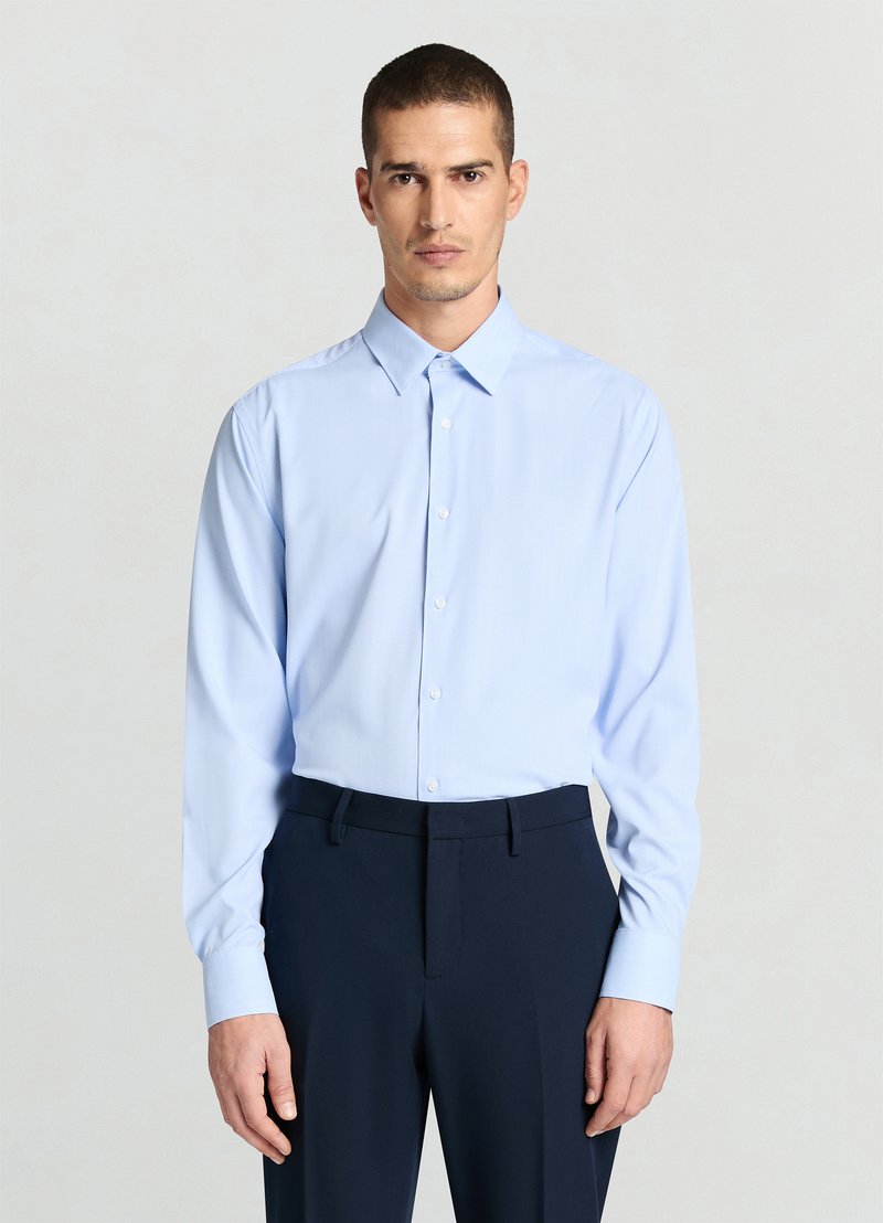 Hellblaues, langärmliges Hemd mit Button-Down-Kragen, das ein dezentes Streifenmuster und eine reguläre Passform aufweist. Kombiniert mit marineblauen Hosen.