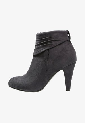 Harmaat mokkanahkaiset nilkkurit, joissa on terävä kärki, nilkassa taitettu yksityiskohta ja korkea piikkikorko. Sileä pinta ja minimalistinen muotoilu.