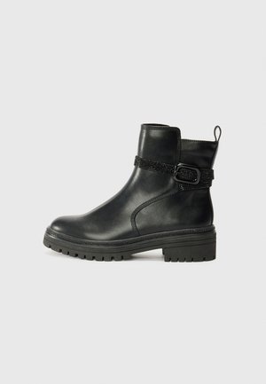 Bottes chelsea en cuir noir avec une semelle épaisse et texturée, dotées d'une sangle décorative avec une boucle et d'un tirant au talon.