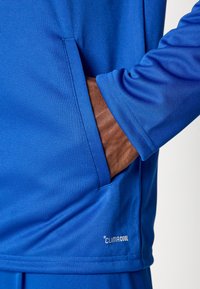 Μπλε αθλητικό μπλουζάκι με τσέπη στο πλάι, κατασκευασμένο από διαπνέον υλικό, με λεία υφή και το λογότυπο "CLIMACOOL" στο τελείωμα.