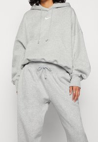 Grå bomullshoodie med en framficka, dragsko på huvan och en liten vit logotyp. Matchas med grå joggers med elastisk midja.