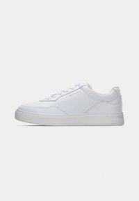 Weiße, flache Sneaker mit Schnürung und goldfarbenem "Tommy Hilfiger"-Logo an der Seite, minimalistisches Design, flache Sohle.