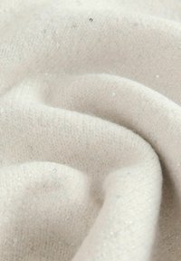 Close-up of soft beige knitted fabric with subtle shimmering fibers and gentle folds.