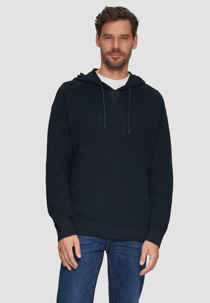 Dunkelblauer Kapuzenpullover aus Rippstrick, mit Kordelzugkapuze, langen Ärmeln und lockerer Passform, kombiniert mit Jeans.