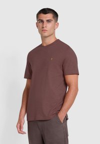 T-shirt in cotone marrone con colletto rotondo, maniche corte e un piccolo logo giallo sul petto. Tessuto liscio e vestibilità comoda.