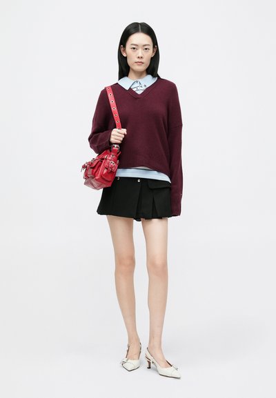 Burgundi oversized pulóver, világoskék galléros ing, fekete pliszírozott mini szoknya és fehér magassarkú cipő. Piros táska részletes hardver díszítésekkel.