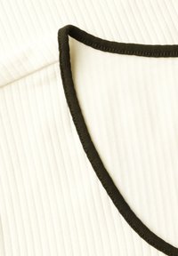 Tessuto bianco a righe con un bordo nero lungo il colletto, caratterizzato da una texture liscia e da linee sottili che si estendono verticalmente.