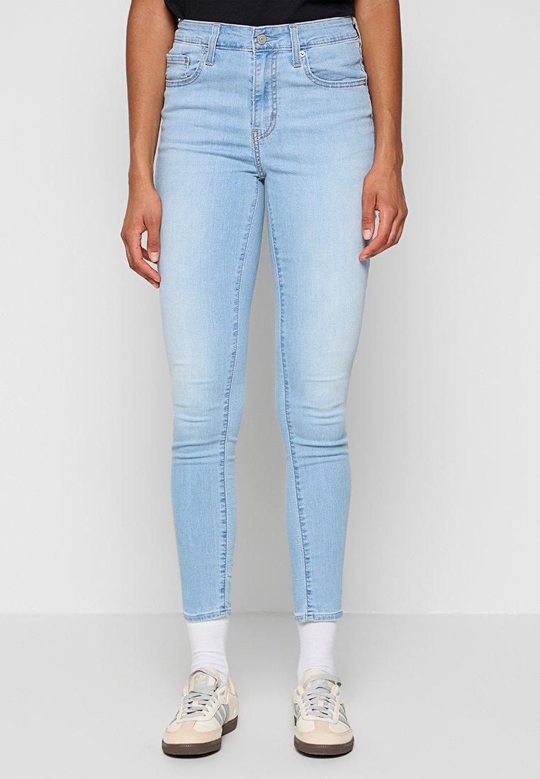 Hellblaue Skinny Jeans aus Denim mit hoher Taille, fünf Taschen und einem ausgeblichenen Finish, kombiniert mit lässigen Schuhen und weißen Socken.