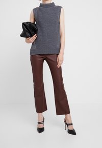 Maglione grigio senza maniche con collo a dolcevita e orlo a coste, abbinato a pantaloni in pelle marrone e una borsa nera intrecciata. Scarpe nere con tacco alto.