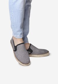 Šedé pletené espadrilky s černými akcenty, s designem na obouvání a jutu na podrážce. V kombinaci se světle modrými džíny.