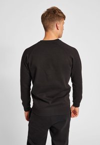 Sort crew neck sweatshirt med raglanærmer, blød stof, ribbede manchetter og bund, styled casual med matchende sorte bukser.