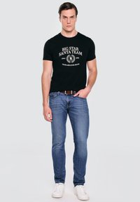 Černé bavlněné tričko s bílým nápisem "BIG STAR SANTA TEAM" a grafickým logem. V kombinaci s světle modrými džíny a bílými teniskami.
