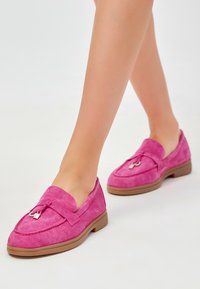 Roze suede loafers met een gestikt ontwerp, decoratieve hardware en een rubberen zool. Rond puntje en zachte textuur zijn opvallende kenmerken.