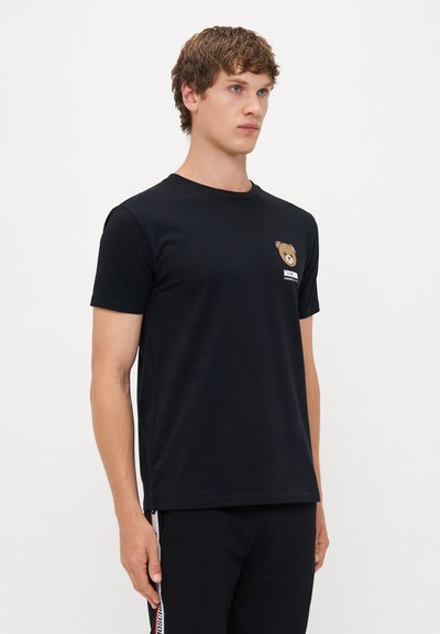 T-shirt de algodão preto com decote redondo, mangas curtas e um pequeno gráfico de um urso na área do bolso do lado esquerdo do peito.