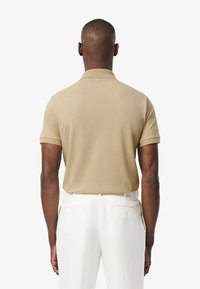Beige kortärmad polo-shirt med en ribbad krage, visad bakifrån, i kombination med ljusa byxor med bakfickor.