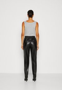 Grijze mouwloze top gecombineerd met zwarte leren broek en high heels. De outfit heeft een relaxte fit en een elastische tailleband.