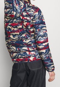 Gewatteerd donzen jack in blauw, rood en crèmekleurig abstract patroon; voorzien van een capuchon en geribbelde textuur met een aansluitend silhouet en ritsen.