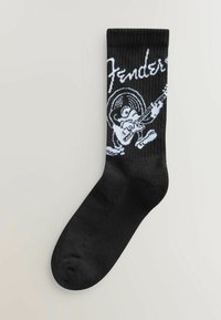 Sosete negre cu logo-ul alb Fender și un personaj de desene animate care cântă la chitară. Fabricate dintr-un material moale și elastic, cu o textură nervurată.
