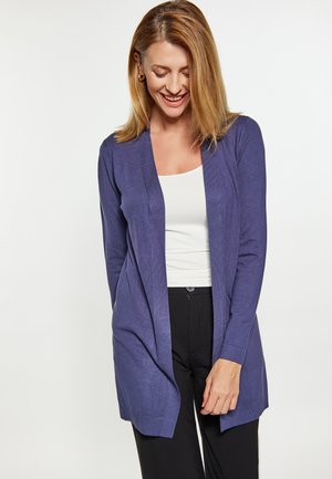 Dlouhá pletená cardigan v tmavě fialové barvě. Otevřený přední design s ribbed manžetami a lemem. Nenošený přes bílý top a černé kalhoty.