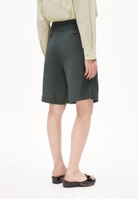 Tmavě zelené šortky s upraveným střihem, s vysokým pasem a bočními sklady, doplněné černými nazouvacími botami a světle zelenou blůzou.