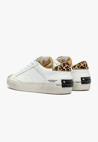 Zapatillas de piel blanca con tacón de leopardo, acentos dorados y suela desgastada. Presentan un diseño de cordones y perforaciones mínimas en los laterales.
