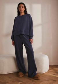 Granatowy, oversize'owy sweatshirt i dopasowane spodnie o szerokiej nogawce wykonane z miękkiego materiału, charakteryzujące się prostym designem i luźnym krojem. Brązowe buty na platformie.