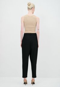 Beige geribbelde mouwloze top gecombineerd met hoge zwarte broeken. De broeken hebben twee achterzakken. Het model draagt beige hakken.