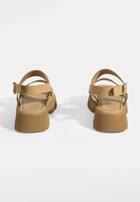 Die sandfarbenen Plattformsandalen verfügen über eine dicke Sohle, zwei schmale Riemen über den Fuß und einen verstellbaren Knöchelriemen mit einer goldenen Schnalle.