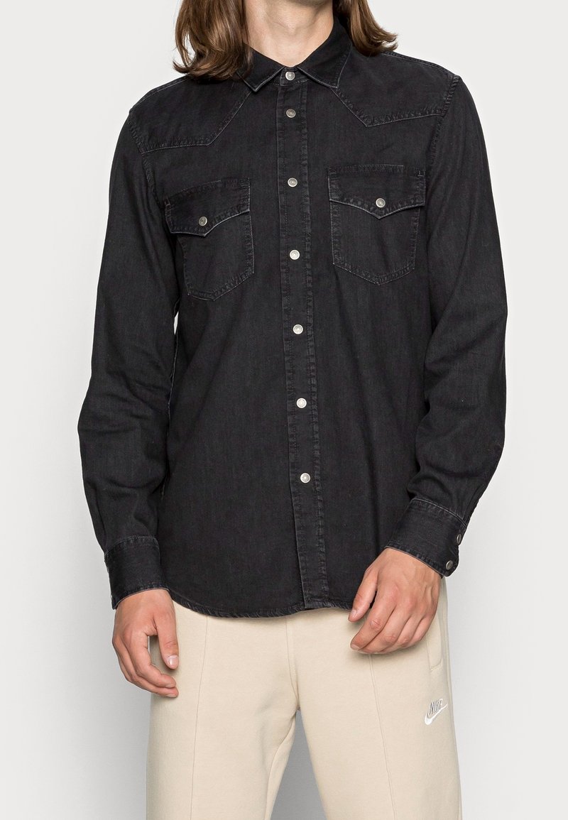 Czarna koszula dżinsowa z zapięciem na zatrzaski, z wyraźnym szewem, dwiema kieszeniami na piersi i długimi rękawami. Gładka tekstura i klasyczny design.