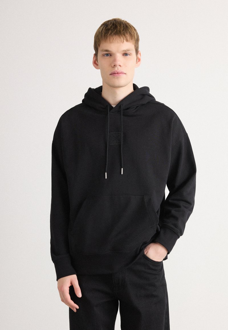Zwarte hoodie van katoenmix, met een voorzak, trekkoorden met metalen uiteinden en een gestructureerde patch op de borst.