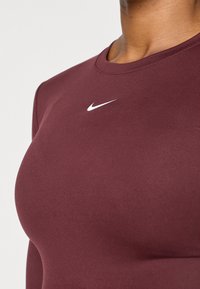 Bordo Nike dugai rukav s prilagođenim dizajnom, okruglim izrezom i bijelim logotipom na prsima. Glatka tekstura, bez vidljivih uzoraka.