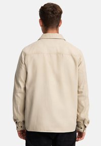 Beige Baumwollhemdjacke mit einem Spitzkragen, langen Ärmeln und Knopfmanschetten. Verfügt über eine glatte Textur und eine lässige Passform.