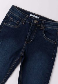 Donkerblauwe spijkerbroek met een klassiek vijf-pocketdesign, zichtbare stiksels en een voorste knoop met reliëfdetails.
