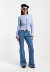 Light blue ribbed long-sleeve top with front buttons, paired with high-waisted flared blue jeans. Accessories include a black beret and sunglasses.