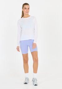 Vit långärmad träningslinne i kombination med ljuslila shorts. Modellen bär grå sneakers och vita ankelsockor. Slät och ventilerande tyg.