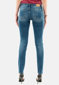 Jeans ajustados de mezclilla azul con cintura de media altura, bolsillos traseros con costura en zigzag y una etiqueta de cuero de marca. Textura suave.