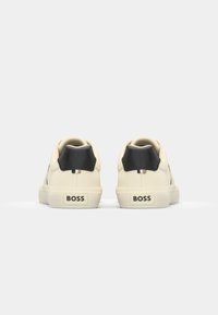 White leather sneakers with a textured finish, black heel accents, and a logo on the heel. Soft sole and understated design.