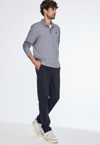 Šedý dlouhý rukáv polo s límečkem, černé kalhoty a neutrální tenisky. Polo má malé logo a volný střih.