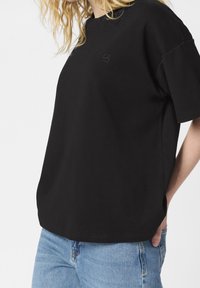 T-shirt nera a maniche corte con scollo rotondo e dettaglio logo ricamato. Tessuto morbido e vestibilità rilassata, abbinata a jeans azzurri chiari.