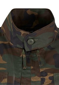 Katonai dzseki magas gallérral, gombos záródással és strapabíró anyagból. Színkombinációja zöld, barna és fekete mintákat tartalmaz.