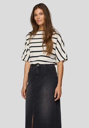 Frau mit langem braunem Haar, die ein weißes Oberteil mit horizontalen schwarzen Streifen und einen hoch taillierten schwarzen Jeansrock mit Frontschlitz trägt.