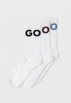 Kolm paari valgeid puuvillaseid sokke soonilise tekstuuriga. Iga sokk on kaunistatud erineva värvi tähtedega, mis kirjavad sõna "GOOO" musta, burgundi ja sinise värviga.