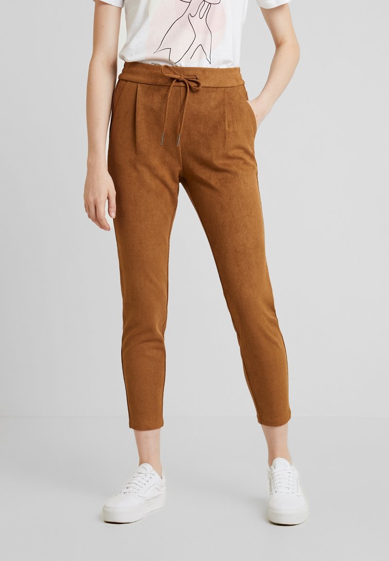 Brown corduroy trousers with a relaxed fit, tapered legs, side pockets, and a drawstring waist worn with white sneakers.