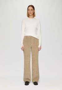 Crème gebreide trui met lange mouwen, gecombineerd met beige corduroy broek met wijde pijpen. Zwarte chunky schoenen maken de outfit compleet.